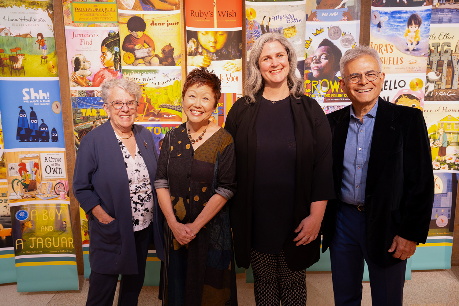 Four people stand side by side in front of a wall covered in images of colorful children's book covers at Elmer L. Andersen Library