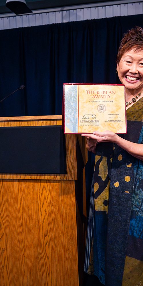 Man stands next to a podium while next to him a smiling woman holds up a certificate that says "The Kerlan Award"