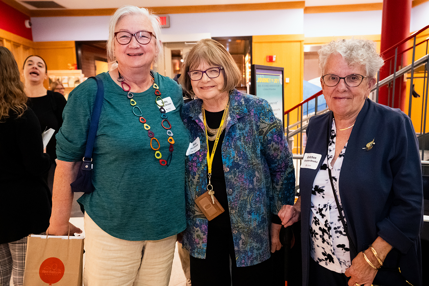 Three smiling women stand side by side in the atrium of Elmer L. Andersen Library at the 2024 Kerlan Award ceremony